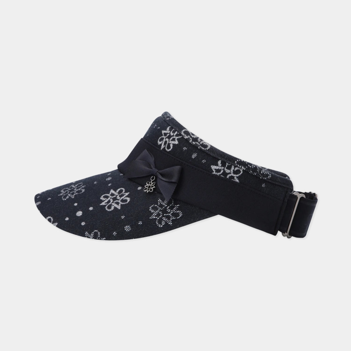 A black visor hat with a white floral bandana print, featuring a black bow and a small gold charm on the front, and an adjustable black strap with a silver buckle at the back, shown against a light gray background.