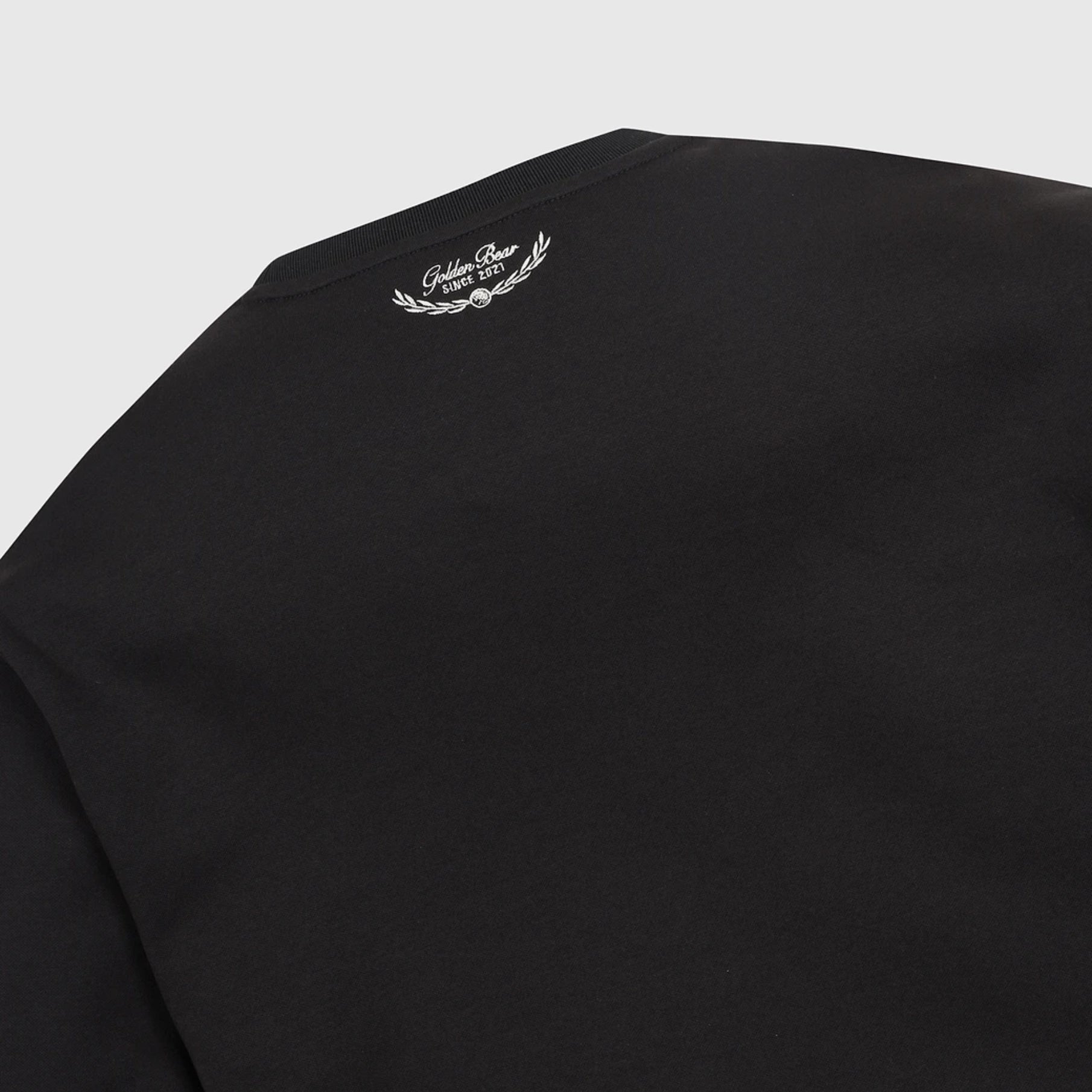 Close-up of a black crewneck sweatshirt showing the inner collar with a white embroidered laurel wreath and 'Golden Bear' logo.
