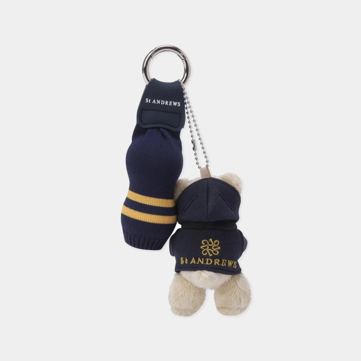 A St Andrews University themed keychain featuring a plush teddy bear wearing a navy blue hoodie with gold lettering, next to a miniature navy blue knit sock with gold stripes and a metal key ring.