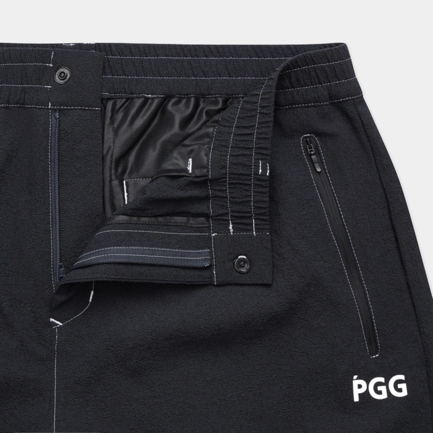 Close-up of black PGG athletic pants showing the interior waistband, elasticized front closure, zippered pocket, and white PGG logo on the lower right leg.