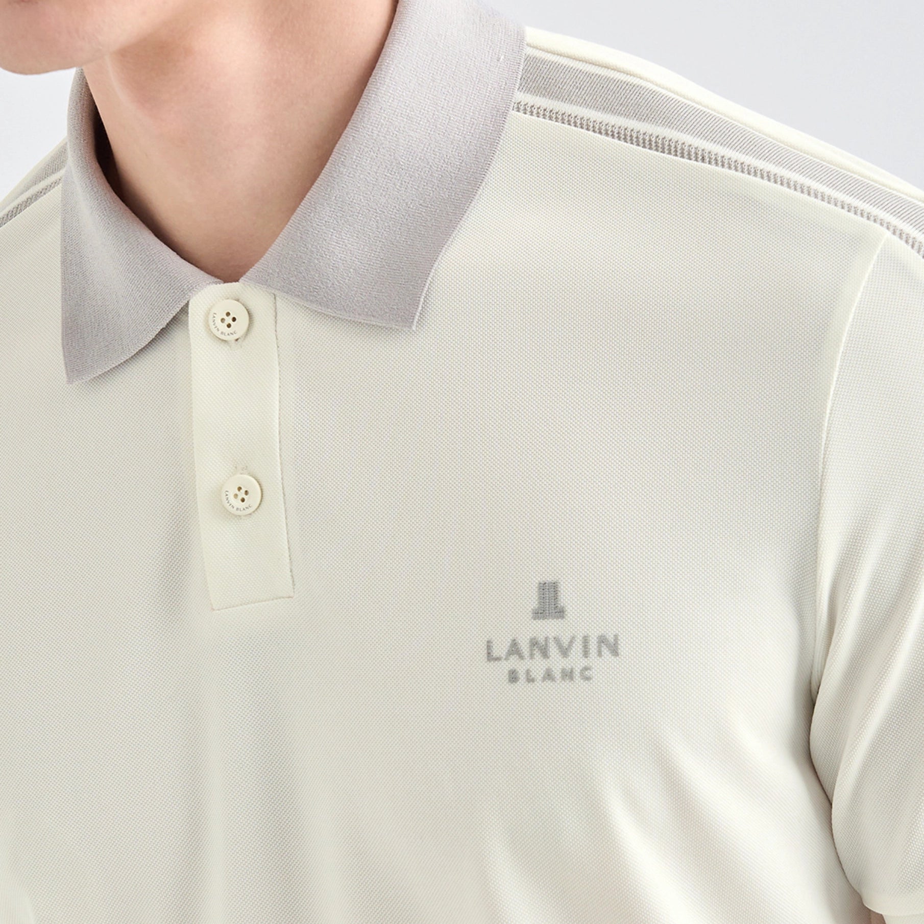 Close-up of a person wearing a light cream/off-white polo shirt with a contrasting light gray collar and subtle gray shoulder stripes. The brand name 'LANVIN BLANC' is printed on the left chest.