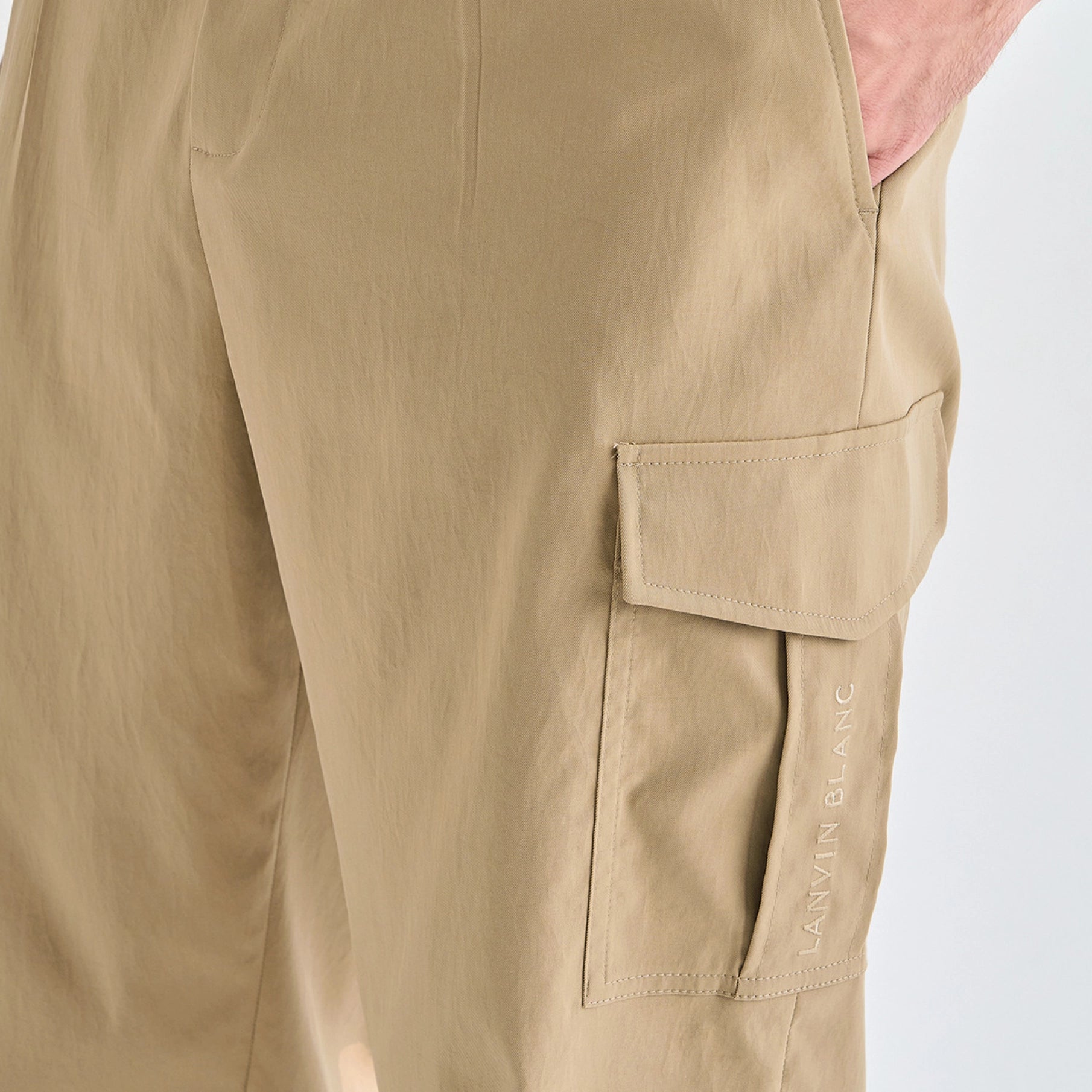 Close-up of a person wearing beige cargo pants, showing a side flap pocket with the brand name 'LANVIN BLANC' printed vertically on the fabric.