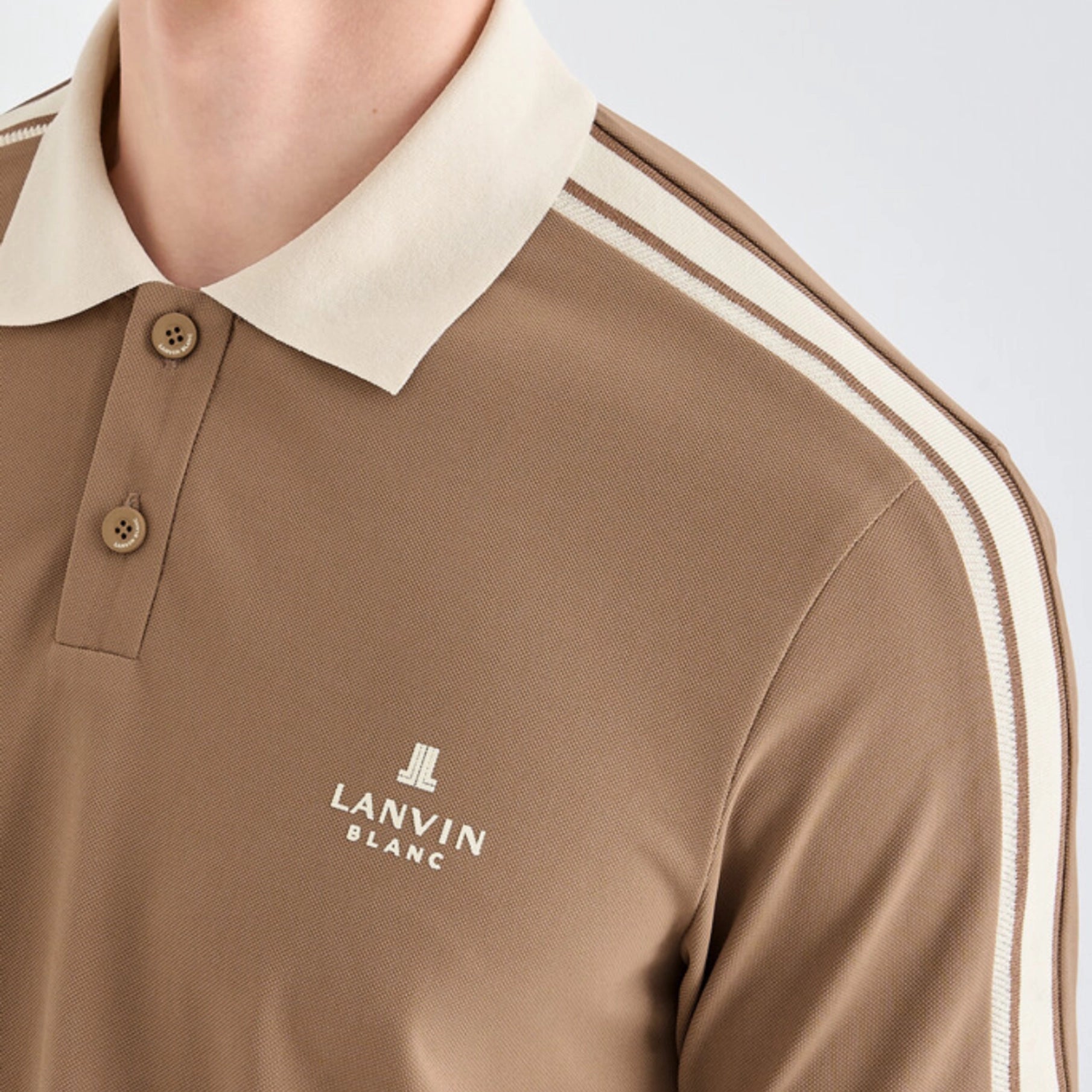Close-up of a person wearing a tan polo shirt with a cream collar and shoulder stripes, featuring the white Lanvin Blanc logo on the chest.