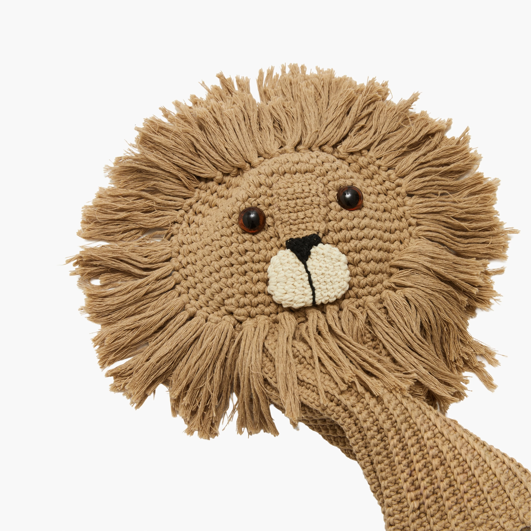 A close-up of a crocheted lion head toy or sock puppet head in warm tan and beige, with dark brown bead eyes, a black nose, and a cream stitched muzzle on a plain white background.