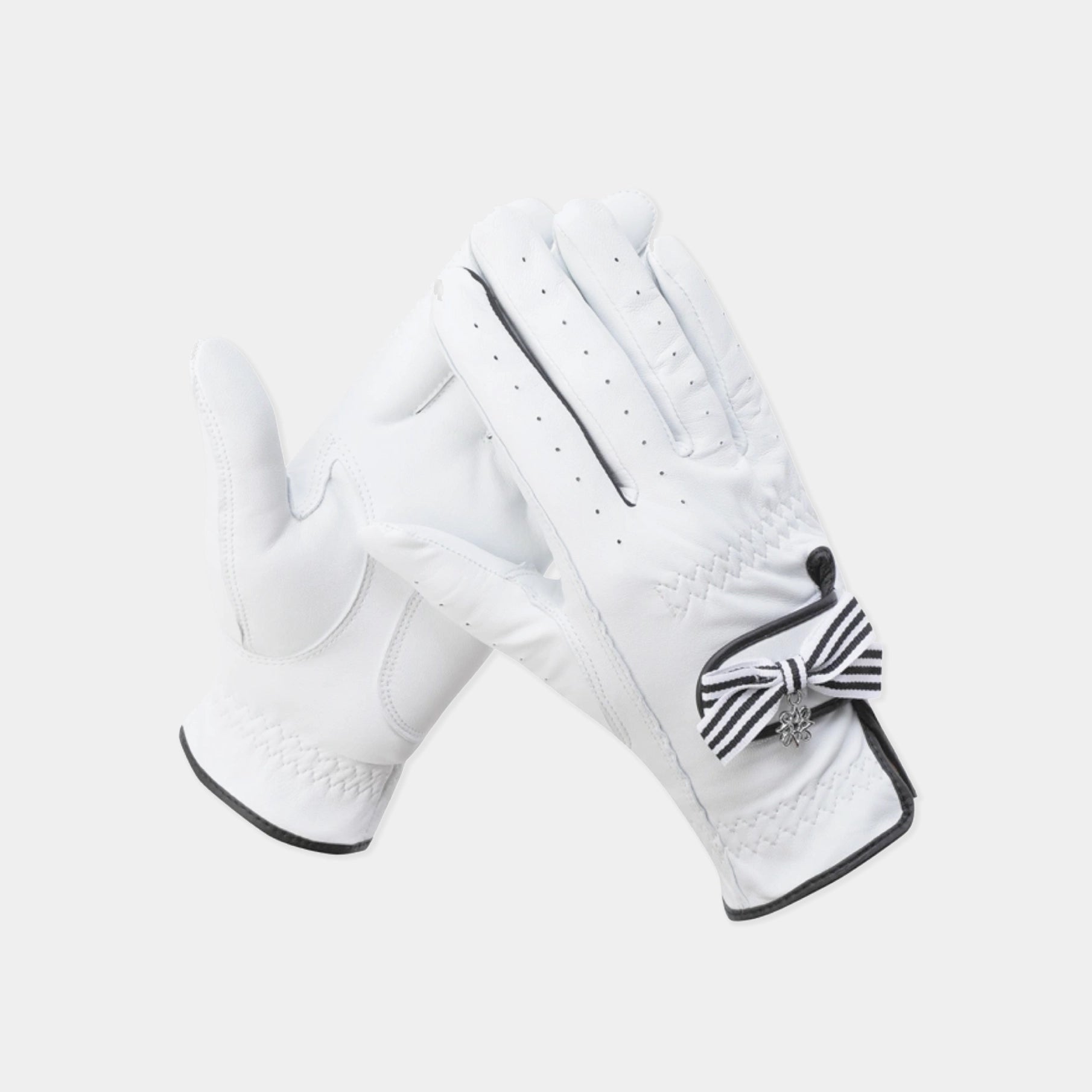 A pair of white leather golf gloves with black trim and a black-and-white striped bow detail on the back of one glove, shown against a light gray background.