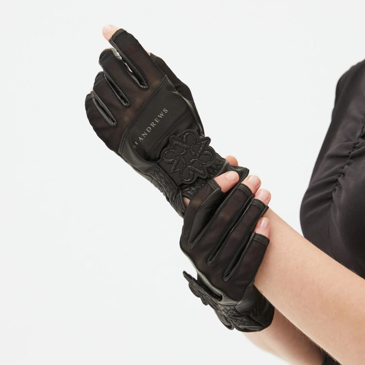 Black leather fingerless gloves with decorative floral embossing on the back, shown being worn on a person's hand against a light gray background.