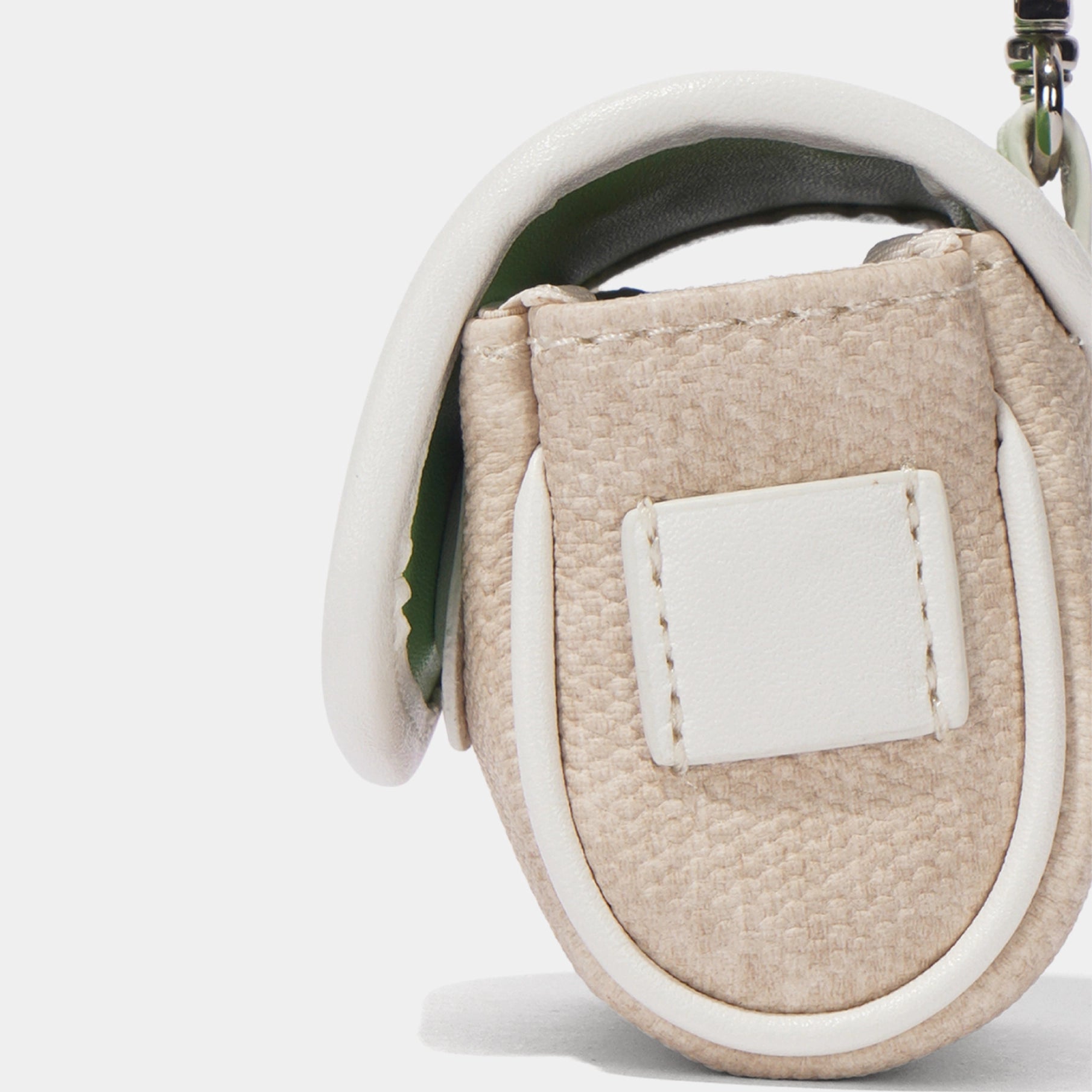 Close-up of a textured beige leather pouch with a white leather trim and a white rectangular patch on the front, shown against a light gray background.