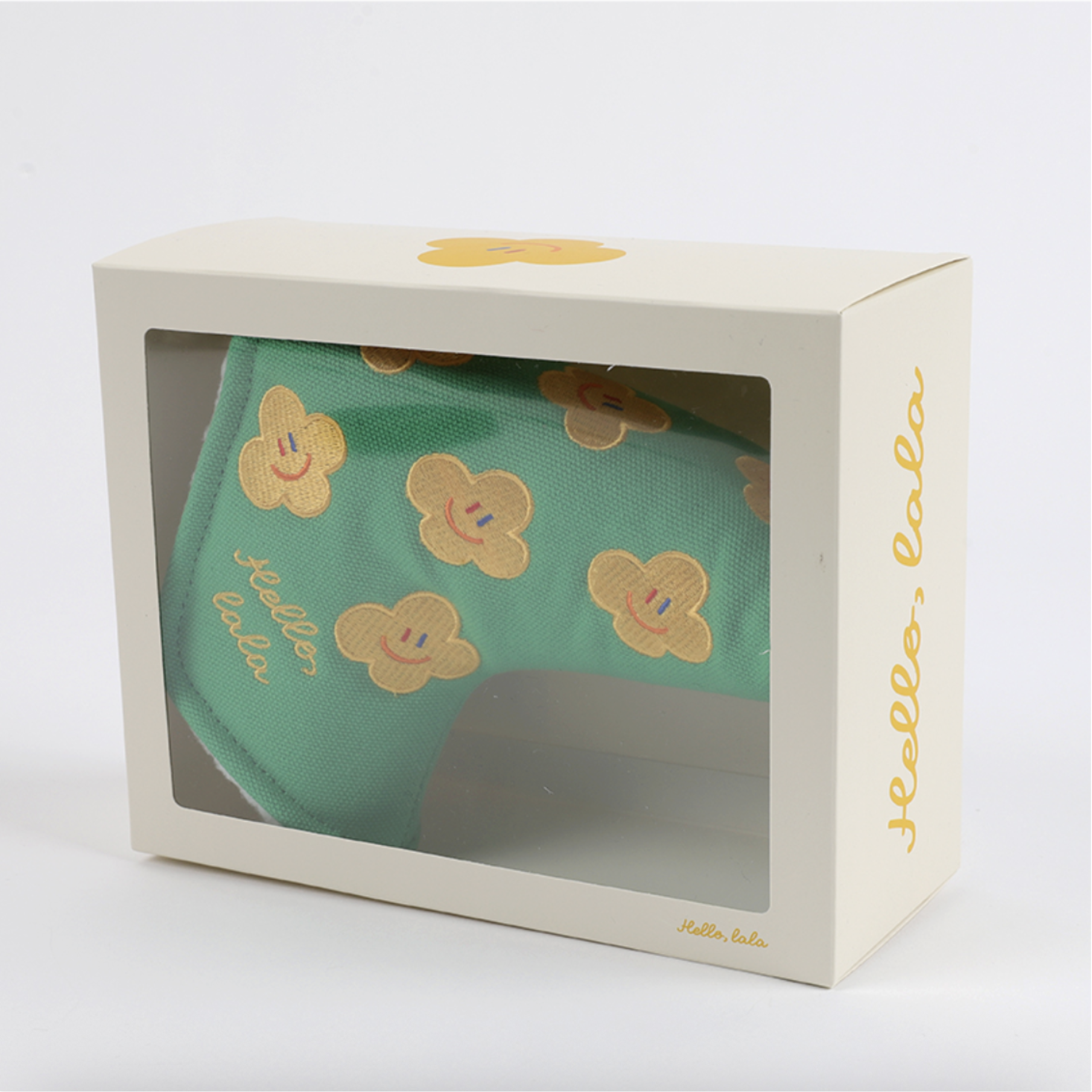 A mint green head cover with embroidered yellow smiley-face flowers, presented inside a cream-colored Hello, Lala gift box with a clear window.