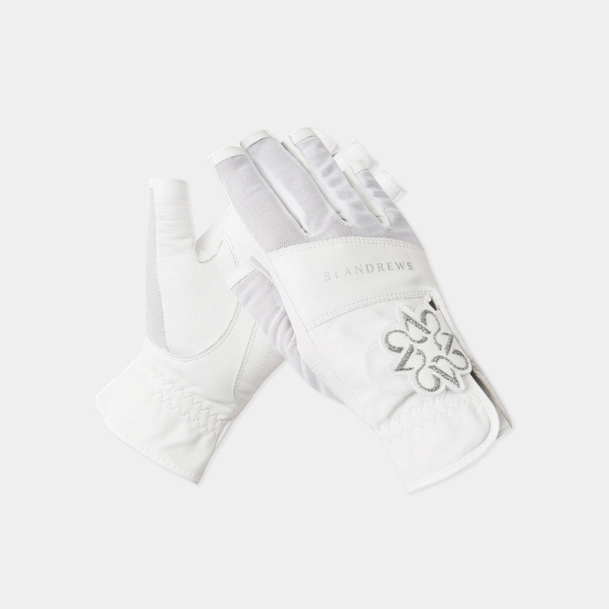 A pair of white equestrian riding gloves by St. Andrews, featuring a silver embroidered monogram logo on the back and a subtle brand name on the wrist strap, set against a light gray background.
