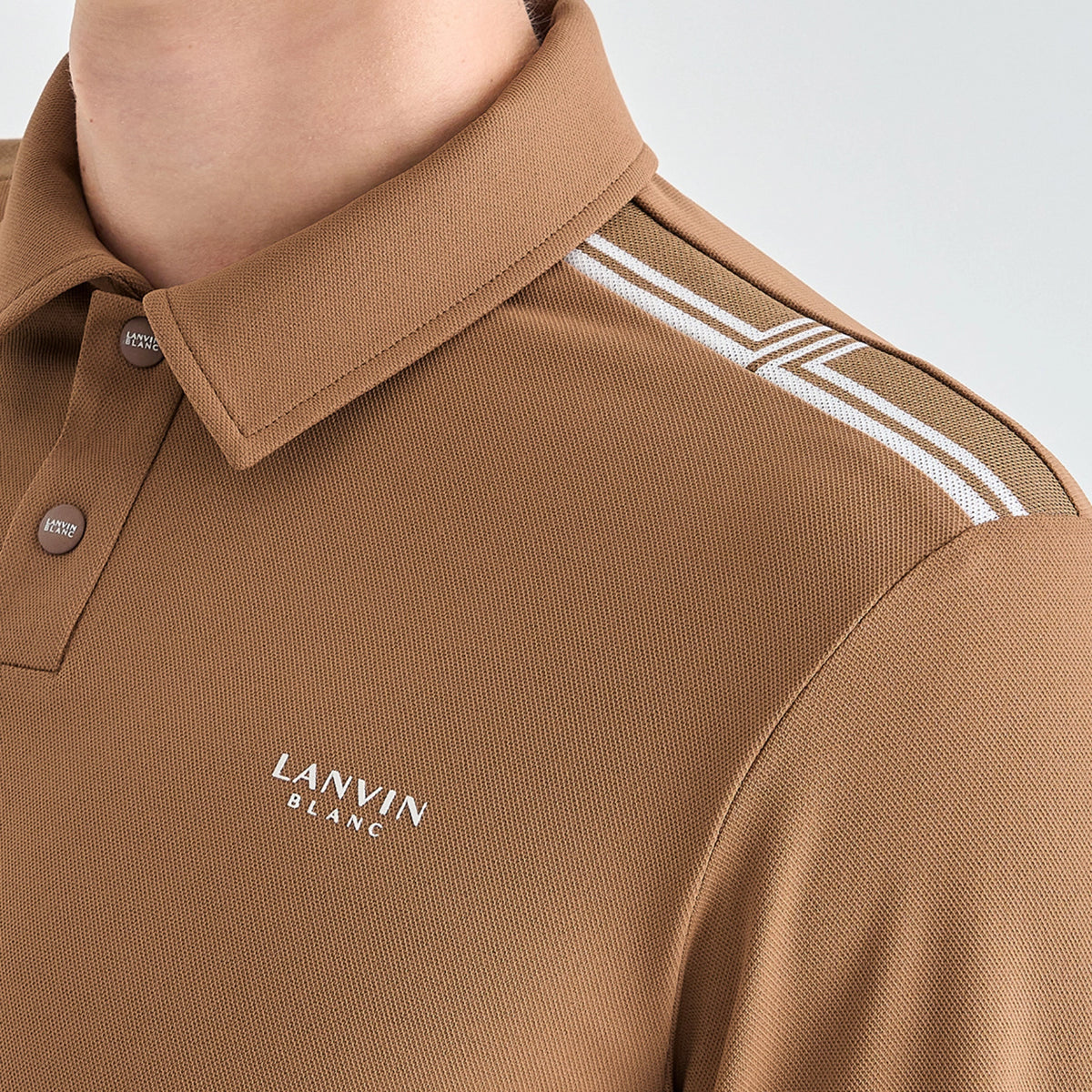 Close-up of a person wearing a tan polo shirt with white double stripes on the shoulder and white 'LANVIN BLANC' text on the chest.