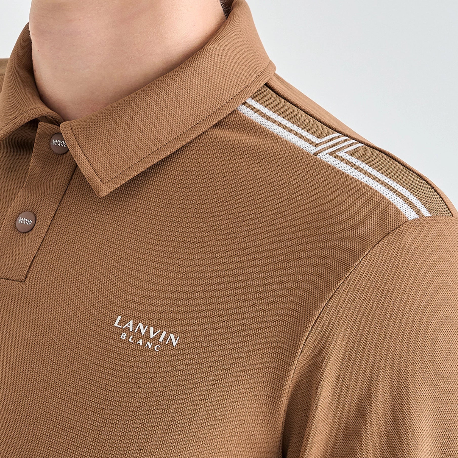 Close-up of a person wearing a tan polo shirt with white double stripes on the shoulder and white 'LANVIN BLANC' text on the chest.