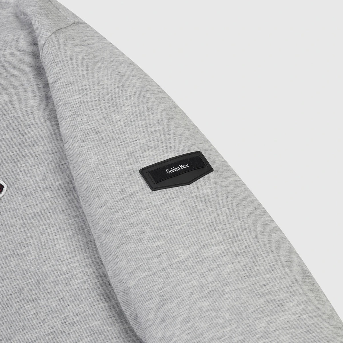 Close-up of a light gray heather sweatshirt sleeve with a black rectangular patch on the cuff featuring the white 'Golden Bear' logo.