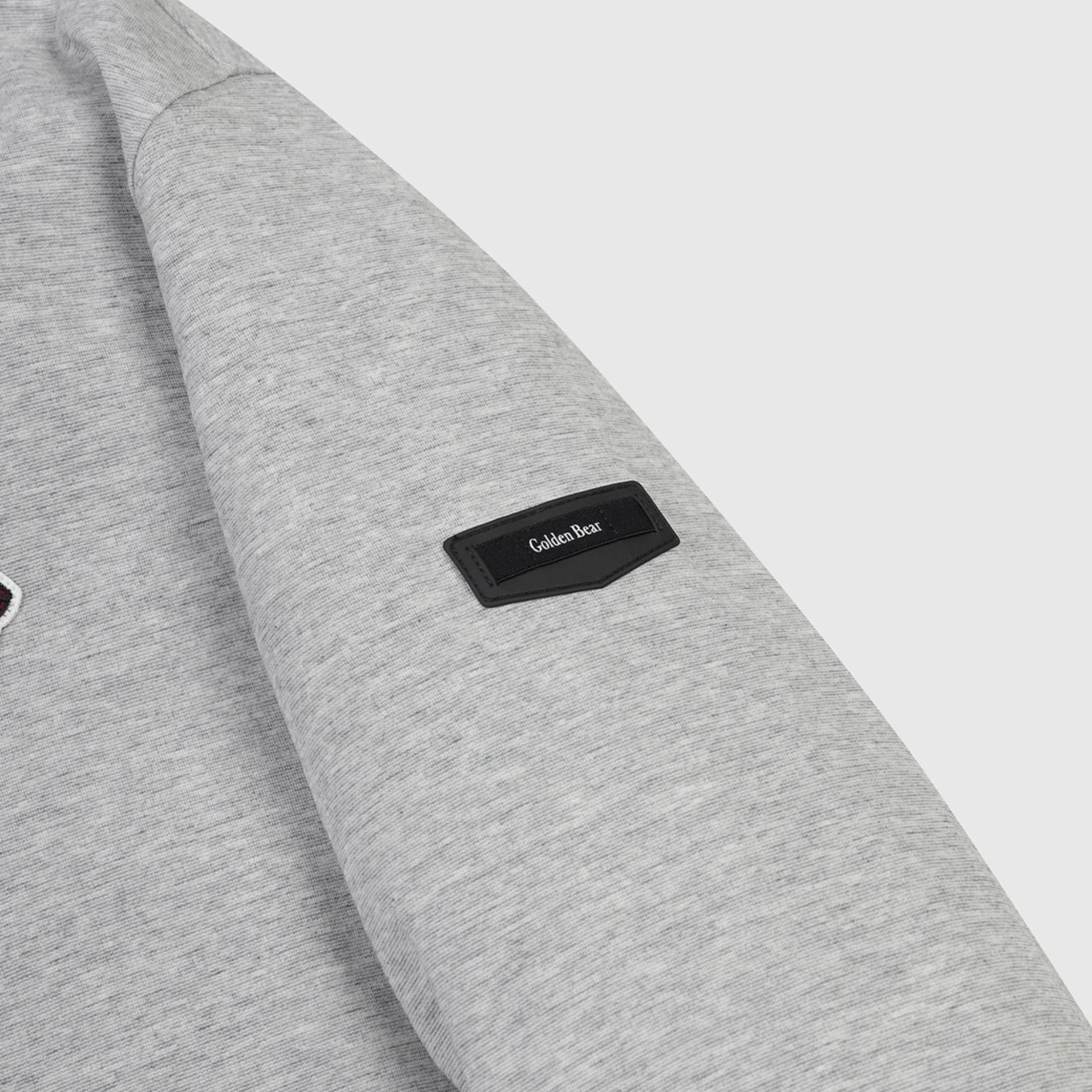 Close-up of a light gray heather sweatshirt sleeve with a black rectangular patch on the cuff featuring the white 'Golden Bear' logo.