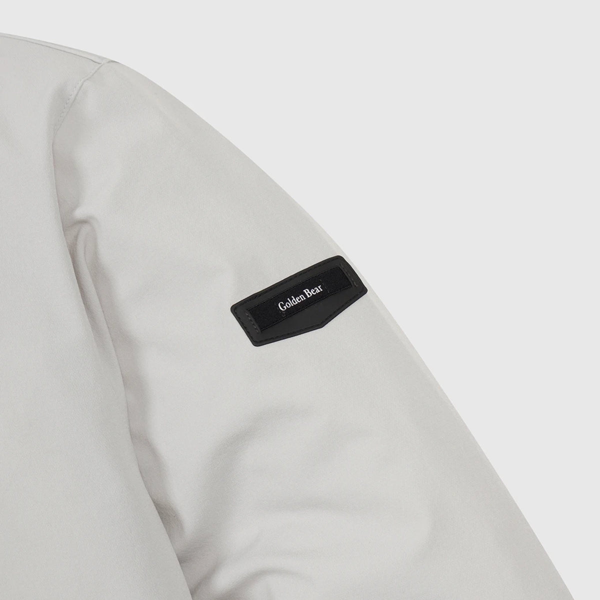 Close-up of a light gray jacket sleeve featuring a black fabric patch with the brand name 'Golden Bear' in white text.
