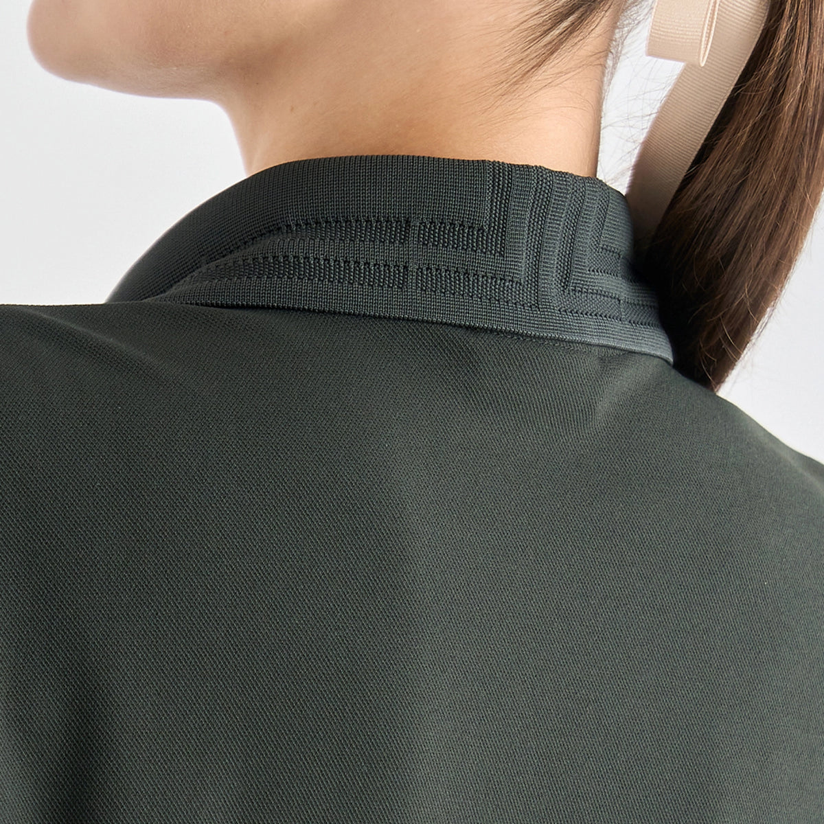 Close-up back view of a person wearing a dark olive green athletic top, showing the collar and textured fabric.
