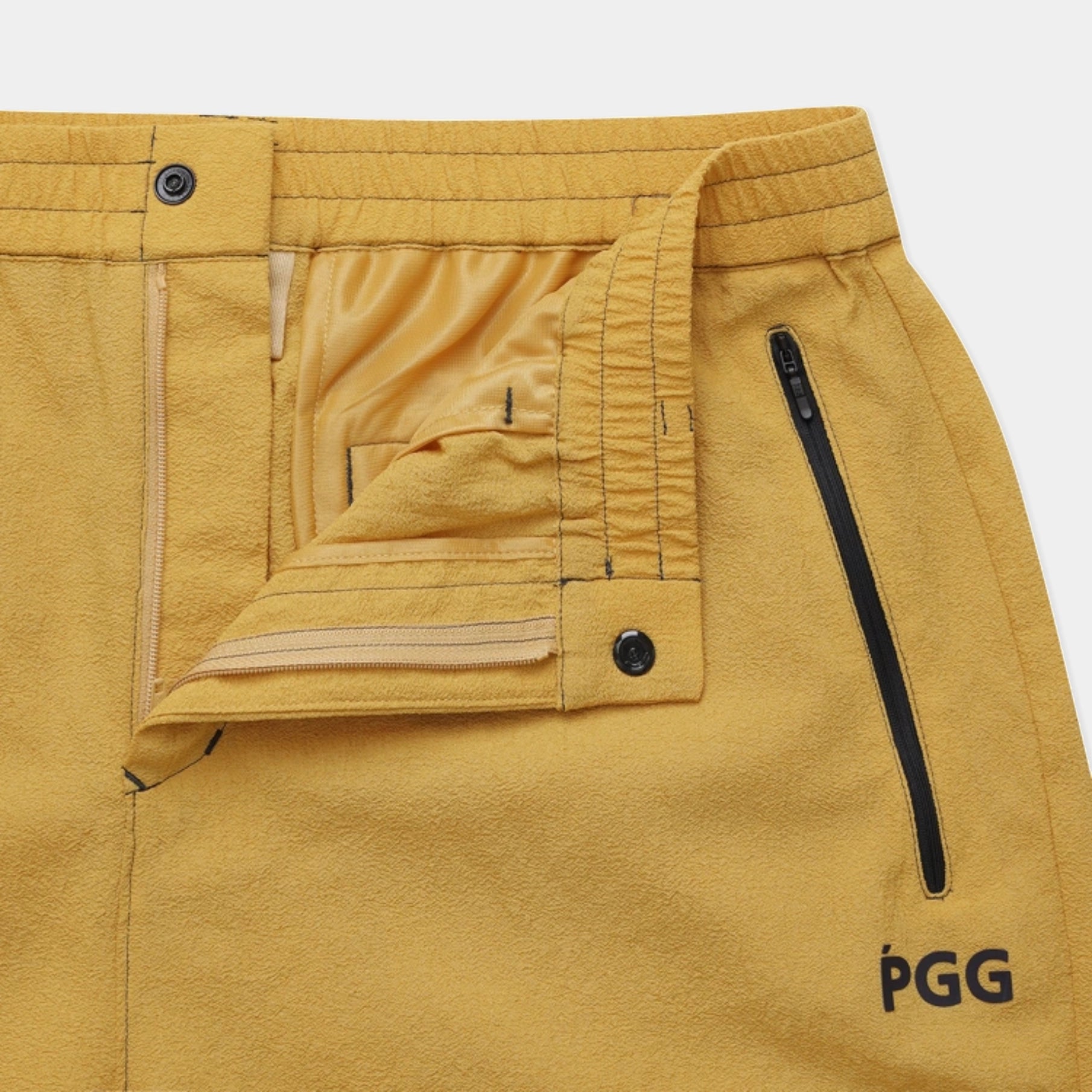 Close-up of a pair of yellow PGG outdoor shorts showing the waistband, interior pocket flap, side zip pocket, and the PGG logo on the lower right leg.