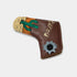 A brown leather golf putter head cover featuring a desert illustration with a green cactus, orange rock, and a silver bullet-shaped patch with a black center, on a light gray background.