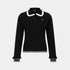 A black long-sleeve polo sweater with a white ruffled collar, white trim at the hem, and white trim at the cuffs, featuring a small embroidered logo on the left chest.