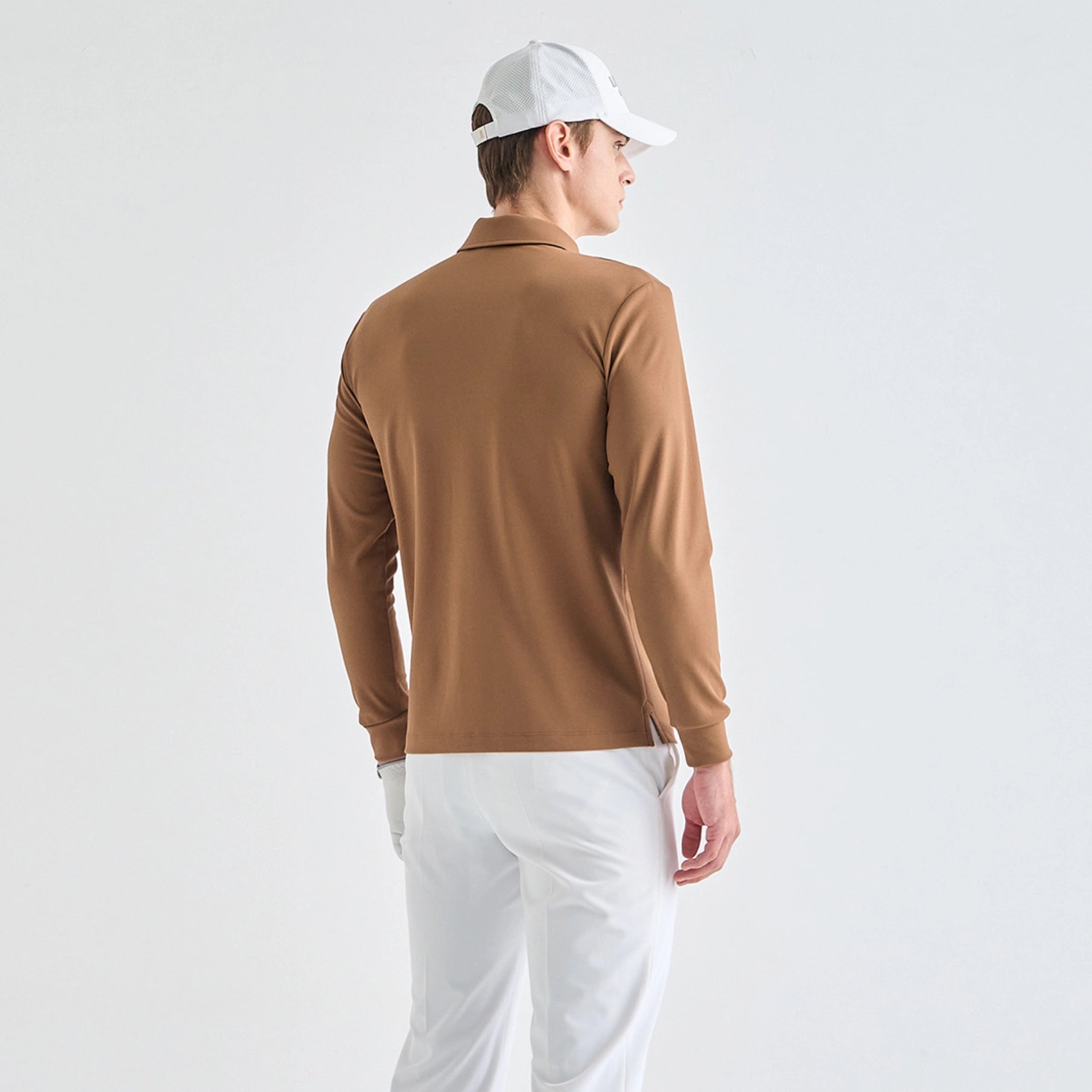 A man wearing a brown long-sleeve polo shirt, white pants, and a white baseball cap, photographed from the back against a clean white studio background.