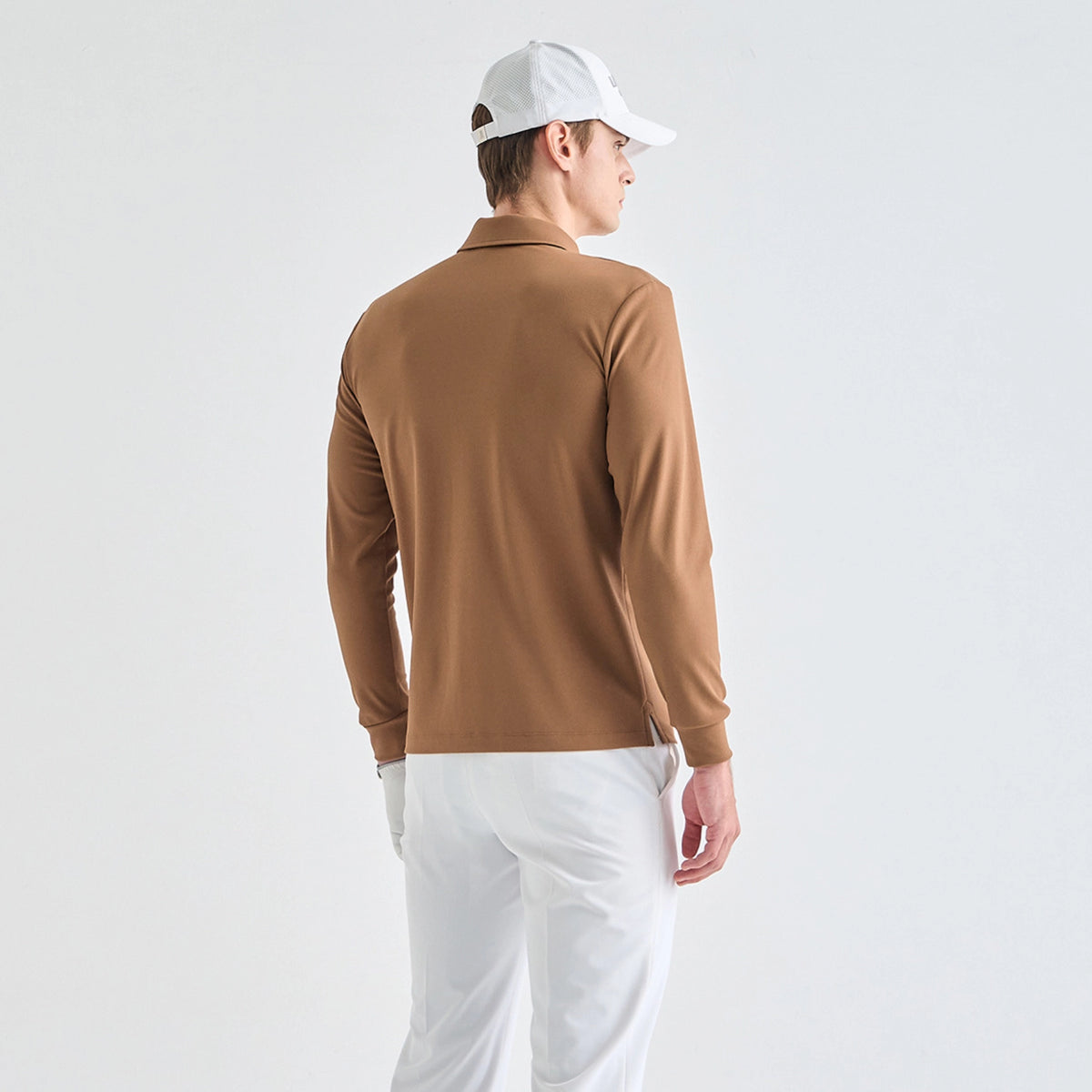 A man wearing a brown long-sleeve polo shirt, white pants, and a white baseball cap, photographed from the back against a clean white studio background.