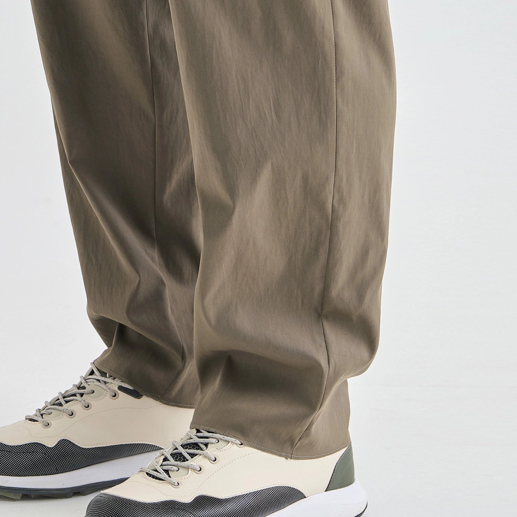 Close-up of a person's legs wearing loose, wide-leg taupe pants and cream and black sneakers against a clean white background.