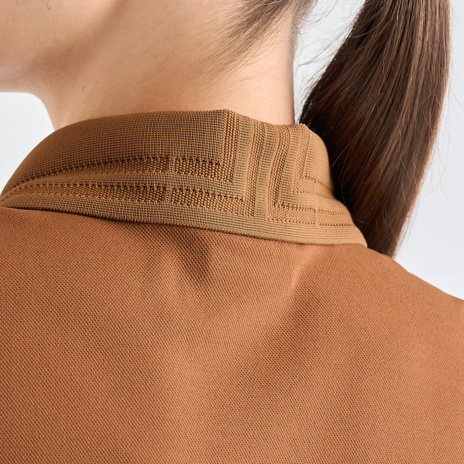 Close-up of a person wearing a brown knit polo shirt, showing the collar and textured fabric against a light gray background.