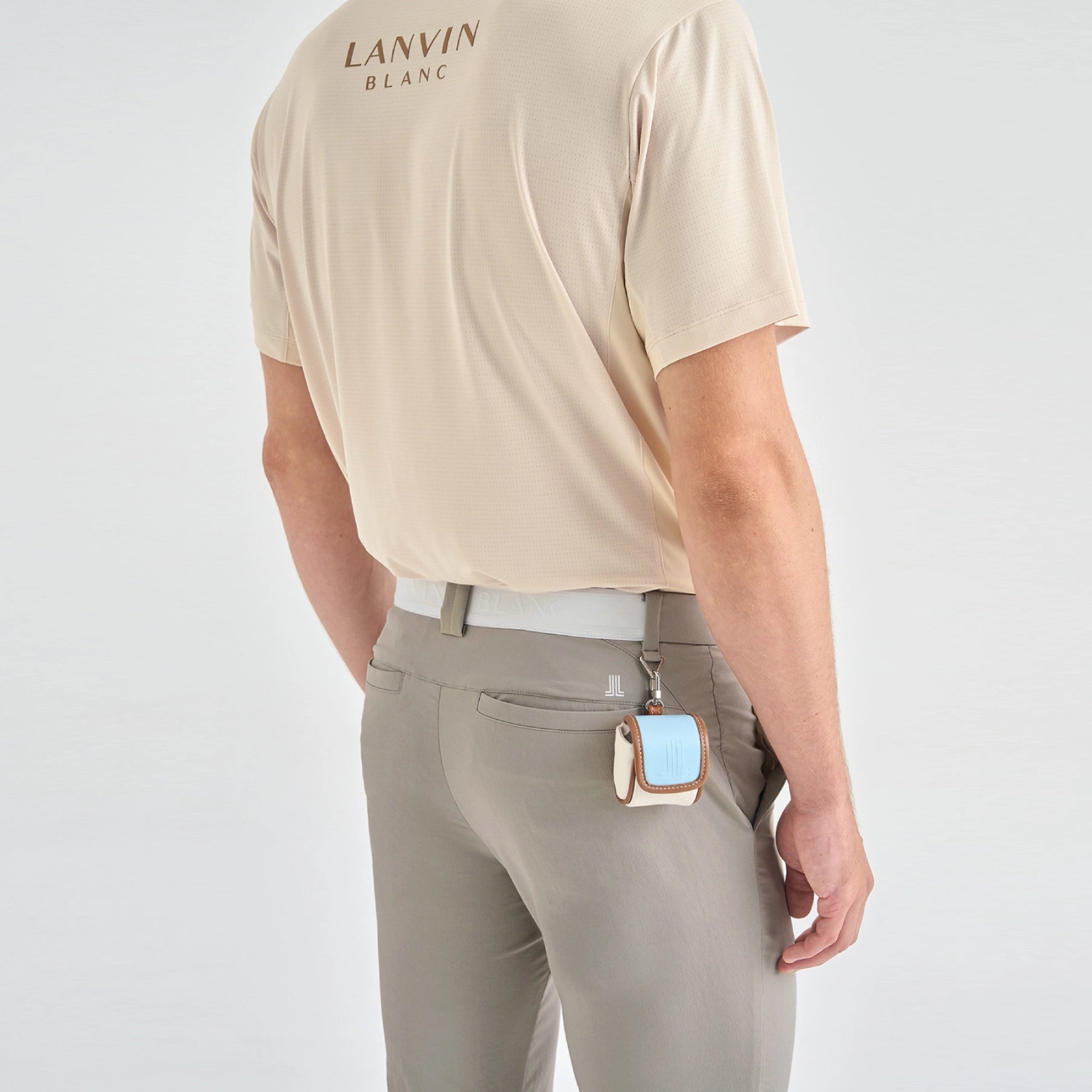 A man shown from the back wearing a beige short-sleeve Lanvin Blanc polo shirt and light gray trousers, with a small light blue and beige accessory hanging from his belt.