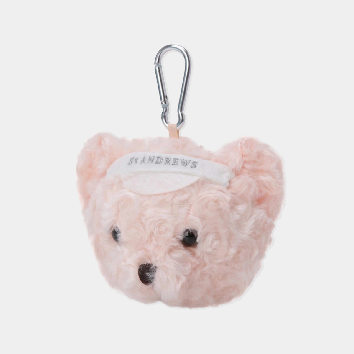 A light pink plush teddy bear head keychain or bag charm with a silver carabiner clip. The bear has curly pink fur, small black eyes, a black nose, and a white headband with the brand name 'ST ANDREWS' printed on it.