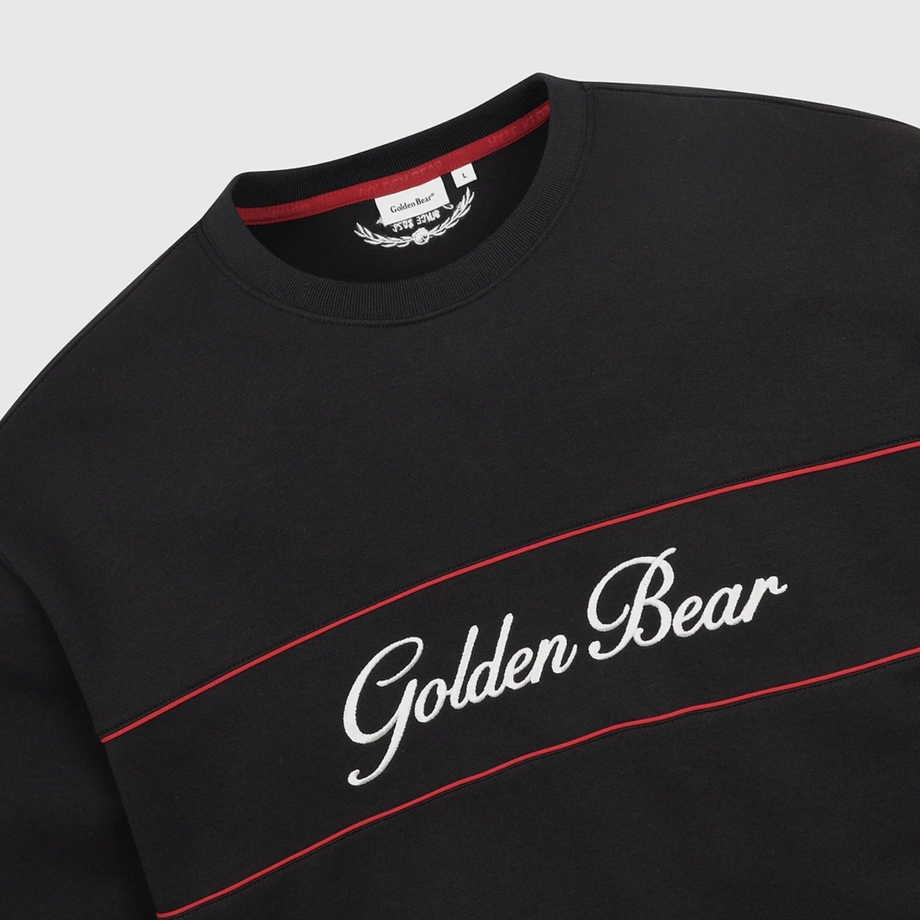 Close-up of a black crewneck sweatshirt with 'Golden Bear' embroidered in white script across the chest, bordered by two thin red lines, on a light gray background.