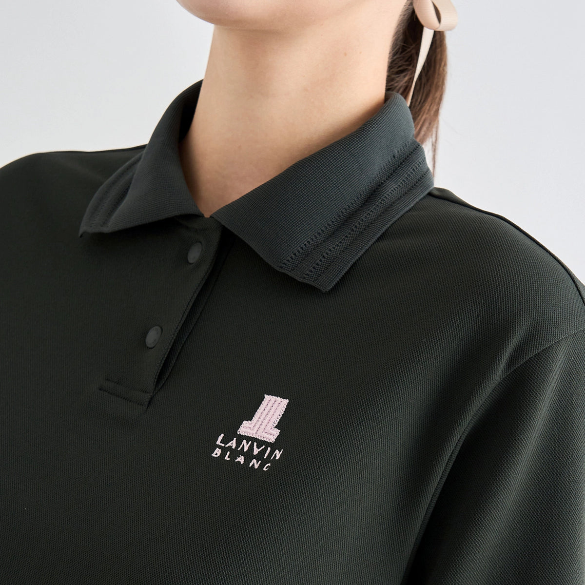 Close-up of a person wearing a dark charcoal gray polo shirt with a small pink and white Lanvin Blanc logo on the left chest.