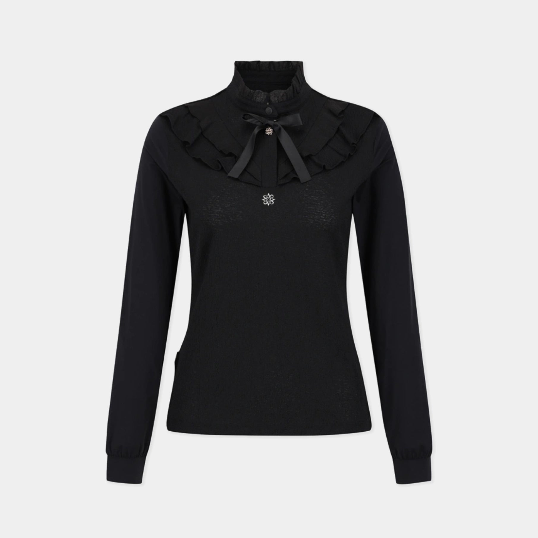 A black long-sleeve knit top with a high mock neck, featuring a layered ruffled collar with a black bow accent and a small silver floral brooch at the center, shown against a light gray background.