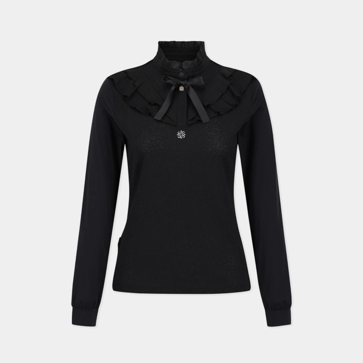 A black long-sleeve knit top with a high mock neck, featuring a layered ruffled collar with a black bow accent and a small silver floral brooch at the center, shown against a light gray background.