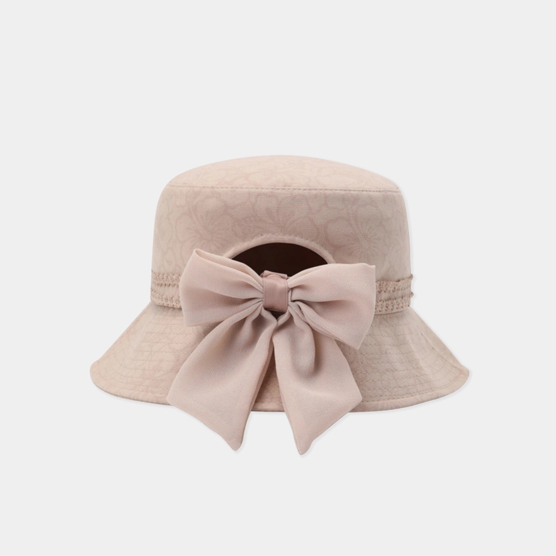 A light beige bucket hat featuring a large matching fabric bow on the front, set against a plain light gray background.