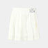 An off-white pleated tennis skirt with a wide waistband and a silver metallic butterfly emblem on the right side, shown against a light gray background.