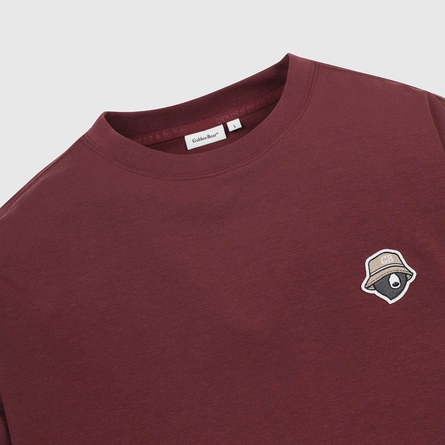 A close-up of a maroon crewneck sweatshirt by Golden Bear, featuring a small embroidered patch on the left chest with a bear wearing a hat.