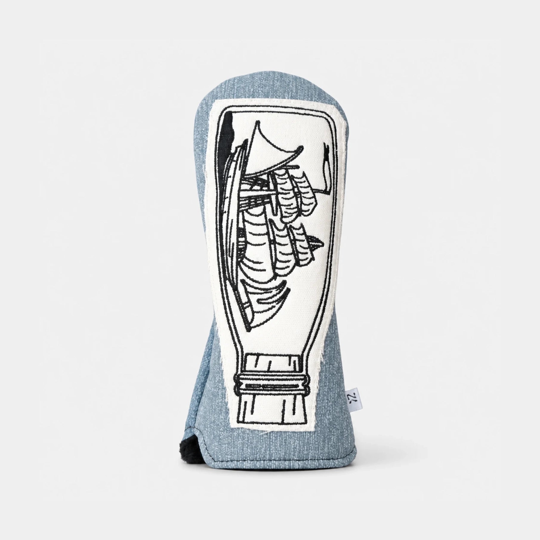 A golf club headcover made of heathered blue denim fabric, featuring a large white rectangular patch with a black line-art illustration of a traditional pagoda. A small white brand tag is visible on the right edge.
