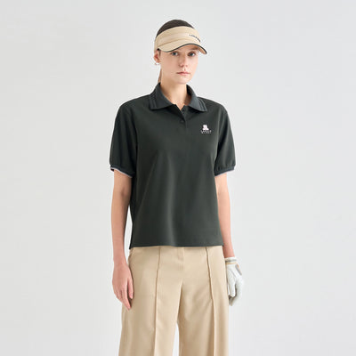 A model wearing a dark olive green short-sleeve polo shirt with a small white embroidered logo on the left chest, paired with beige pants, a beige visor, and a white golf glove, against a light gray studio background.
