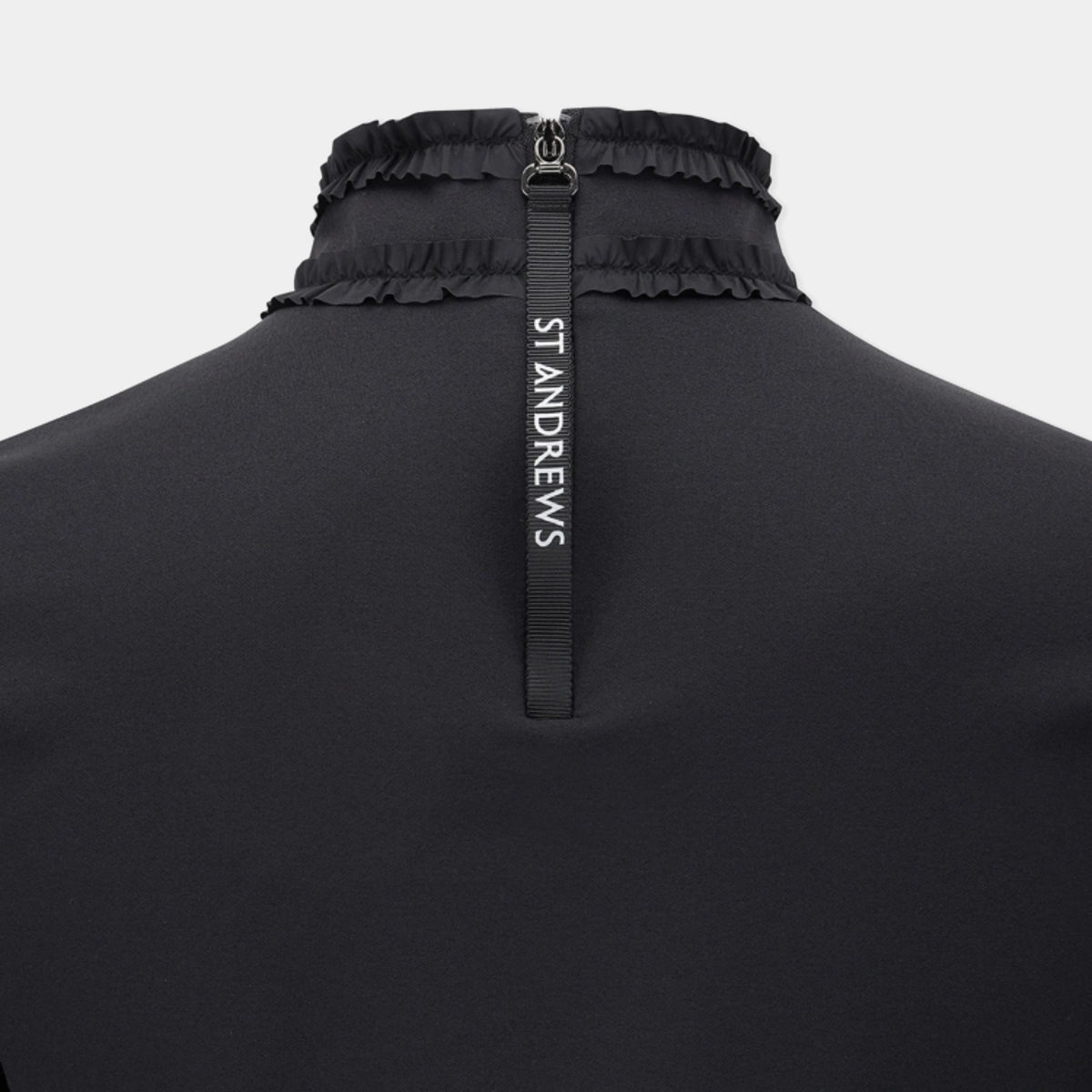 Close-up of the back of a black St Andrews athletic top, featuring a high gathered collar with a central black zipper pull tab printed with the brand name 'ST ANDREWS' in white.