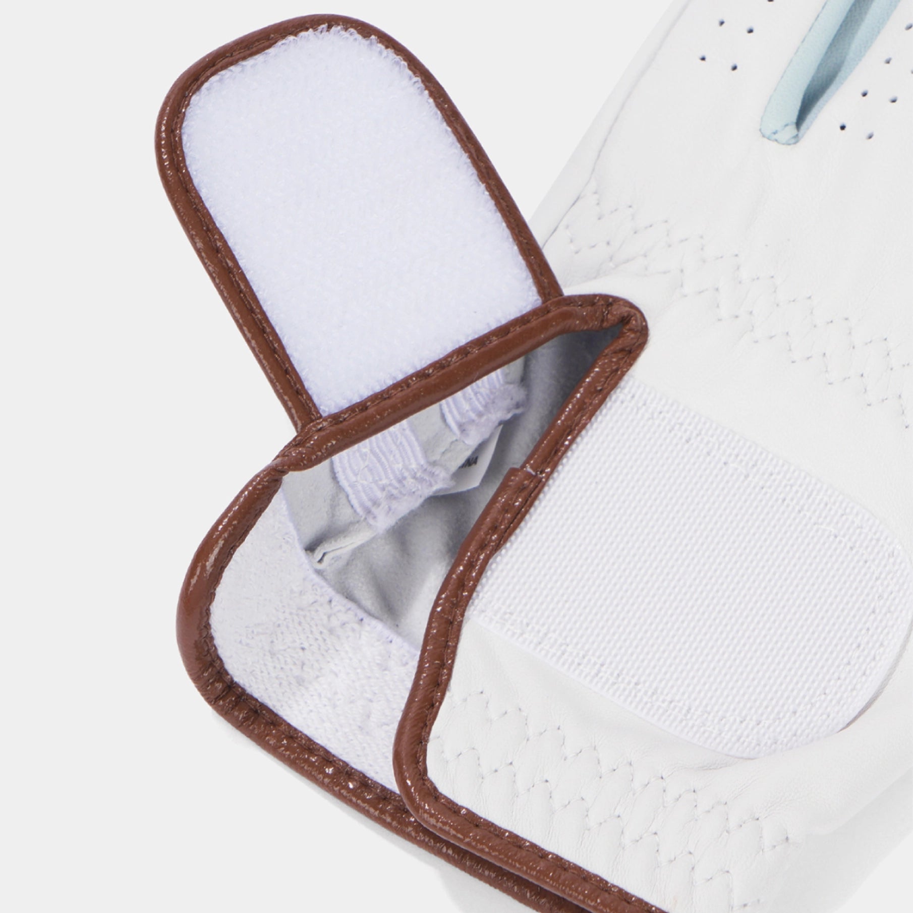 Close-up of a white golf glove showing the textured palm, a brown stitched trim, and a white hook-and-loop fastening flap.