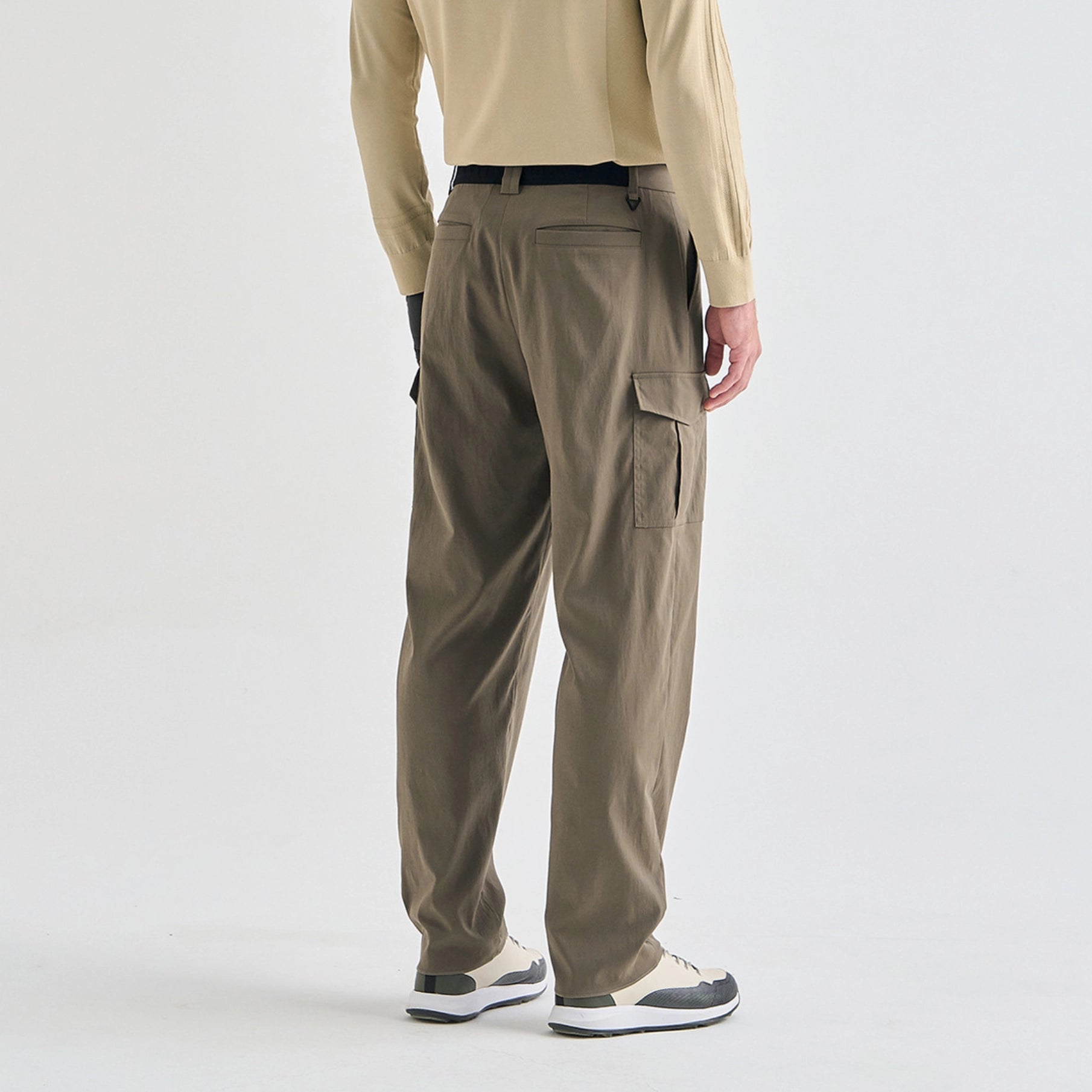 A person shown from the back wearing olive brown cargo pants, a beige long-sleeve shirt, and sneakers against a clean white studio background.