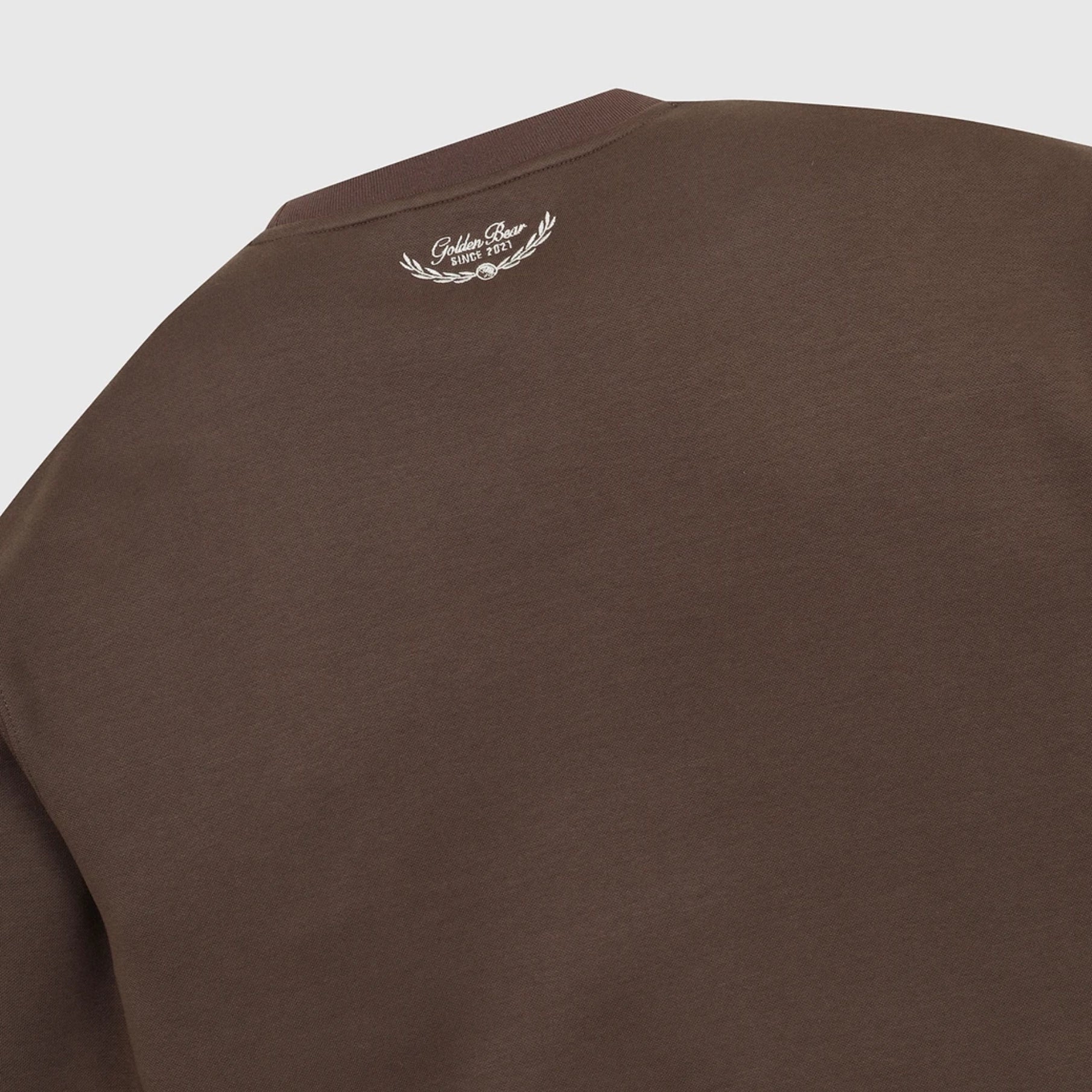 Close-up of a brown crewneck sweatshirt showing the inner neck label with a white laurel wreath logo.