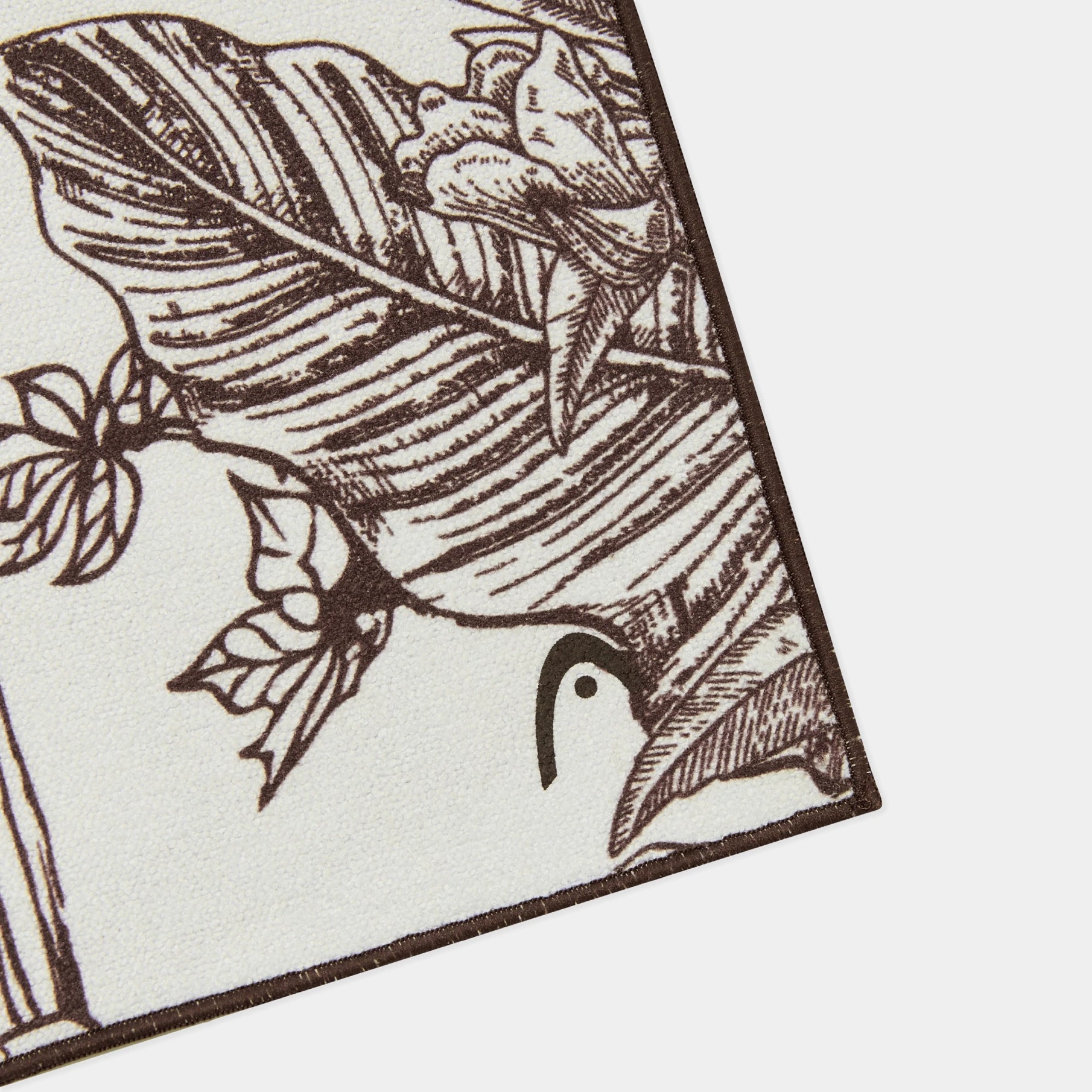 A close-up of a rectangular textile or print with a brown botanical line drawing on an off-white background, shown at an angle against a white backdrop.