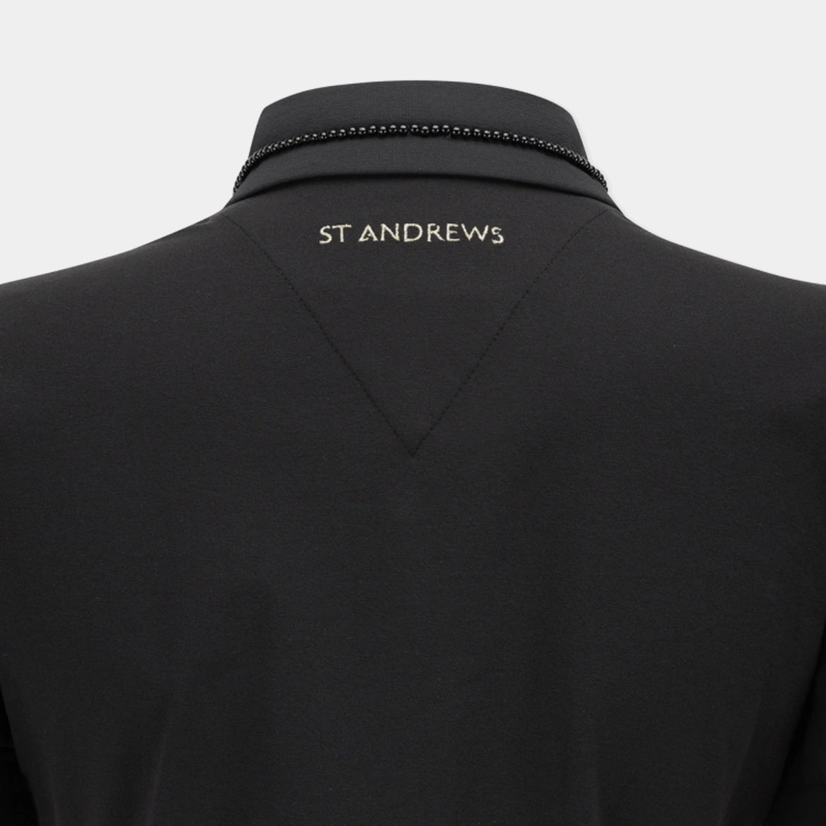 Close-up back view of a black St Andrews polo shirt on a mannequin, showing the brand name 'ST ANDREWS' in gold lettering on the upper back and a decorative black beaded trim along the collar.