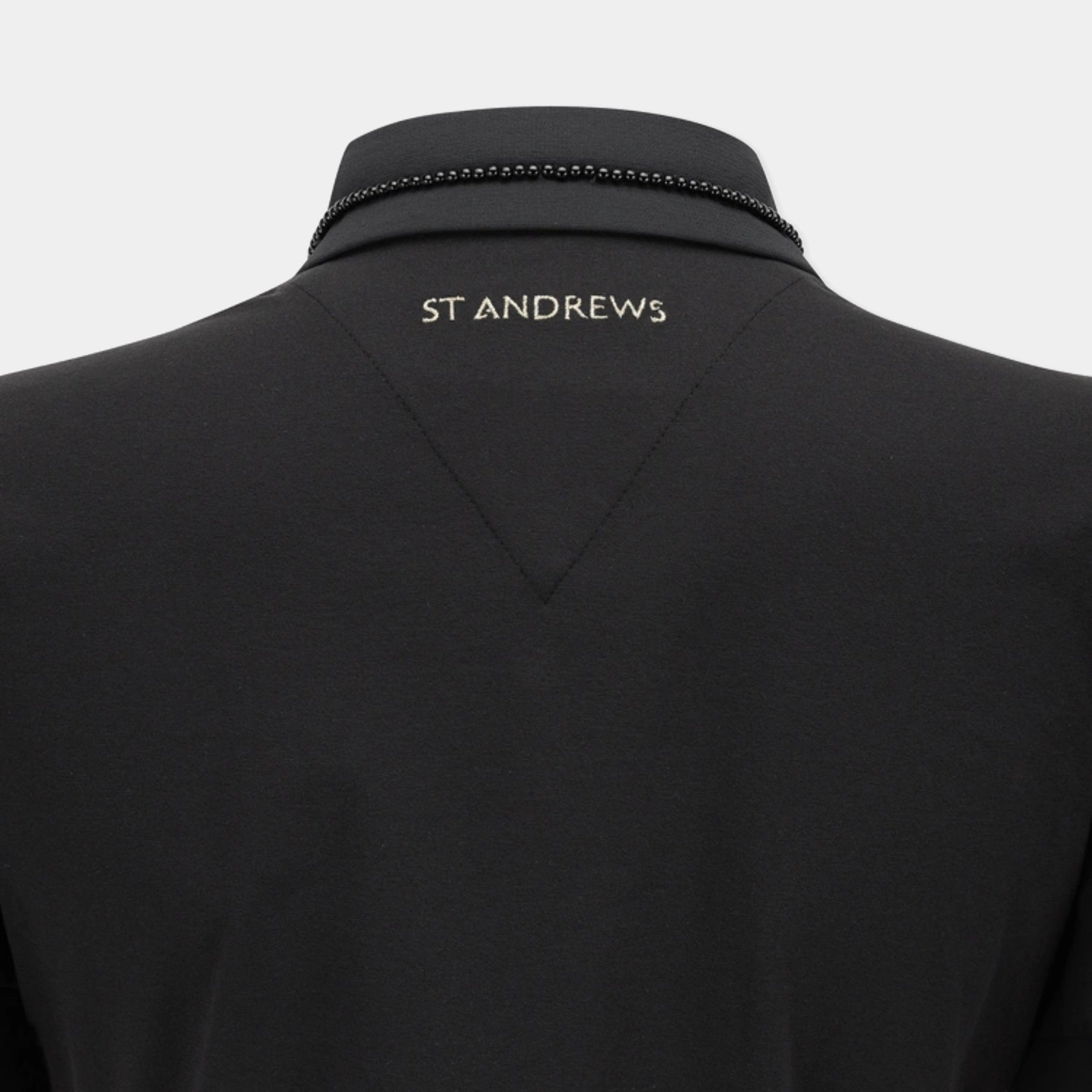 Close-up back view of a black St Andrews polo shirt on a mannequin, showing the brand name 'ST ANDREWS' in gold lettering on the upper back and a decorative black beaded trim along the collar.