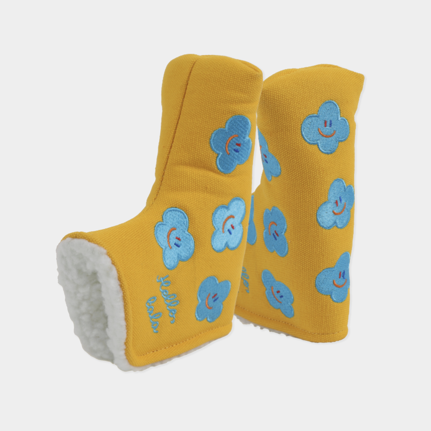 A pair of yellow knit head covers with a white sherpa lining, decorated with blue embroidered smiley-face clouds. One boot is shown standing upright while the other lies on its side to display the white lining.