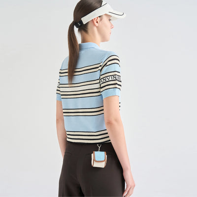 A woman shown from the back wearing a light blue short-sleeve knit polo shirt with black and beige horizontal stripes, a white visor, and dark brown pants. The brand name 'MARVIN B.