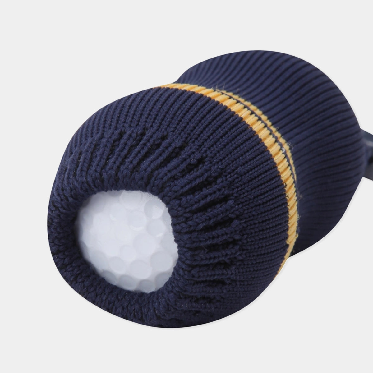 A close-up of a navy blue golf club headcover with a ribbed knit texture and a thin gold stripe, shown with a white golf ball inside on a light gray background.