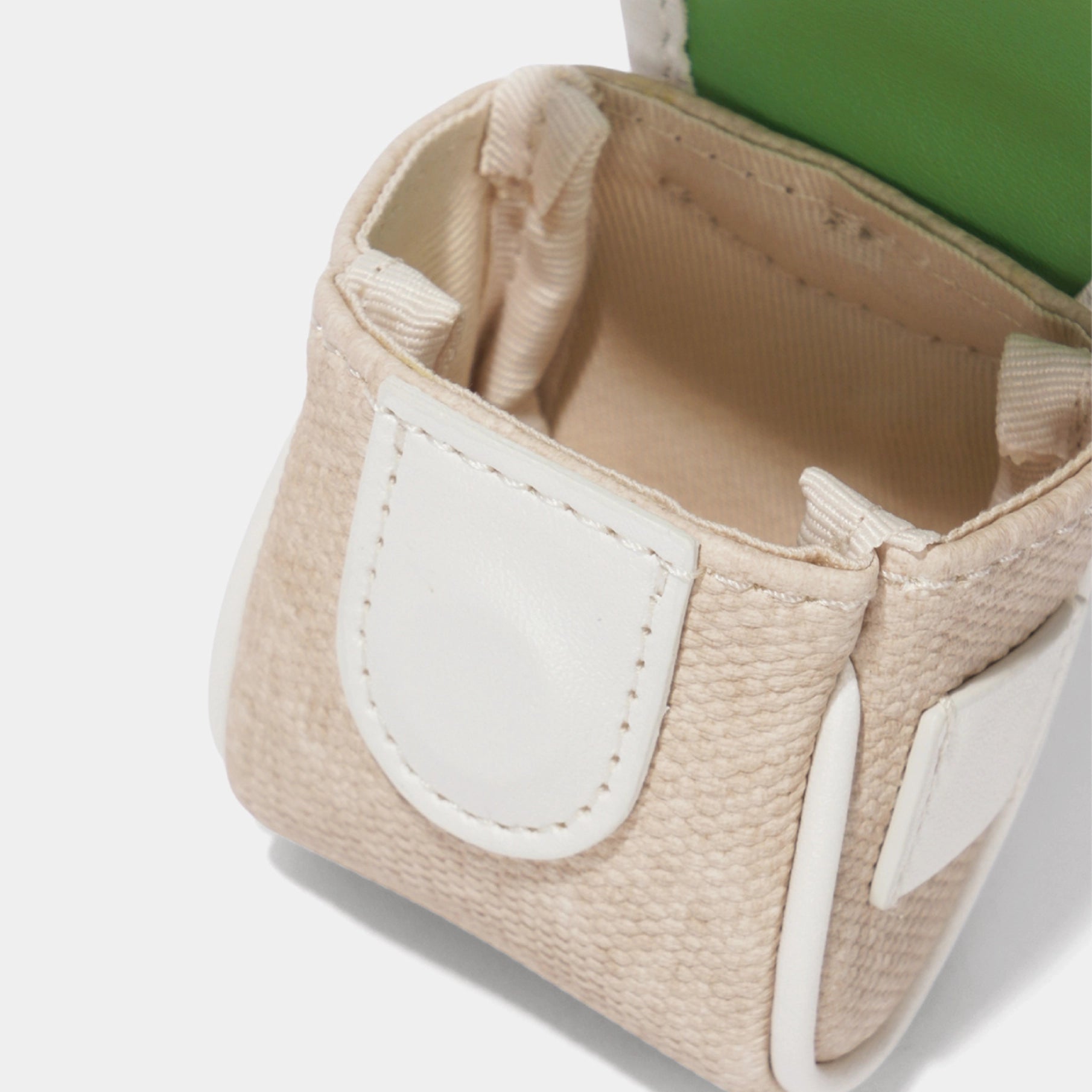 Close-up of a small textured beige bag with white trim and a green interior lining, shown on a clean white background.
