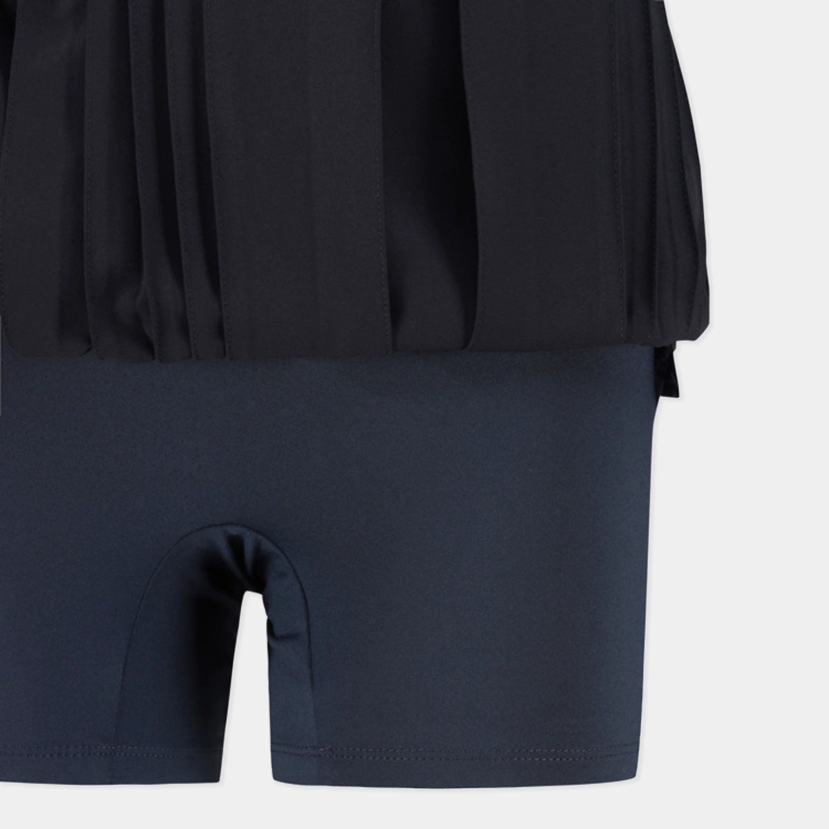 Close-up of a dark navy athletic outfit showing a pleated black top and matching high-waisted shorts with a built-in pouch.