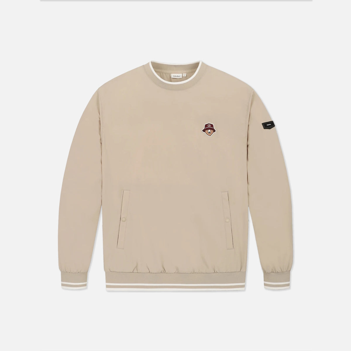 A beige crewneck sweatshirt with a small embroidered character patch on the left chest and a black brand patch on the right sleeve, displayed on a clean white background.